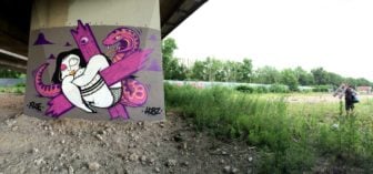 The artists Floe and Hobz can be seen leaving the scene of this graffiti mural, carrying their art supplies and painting tools